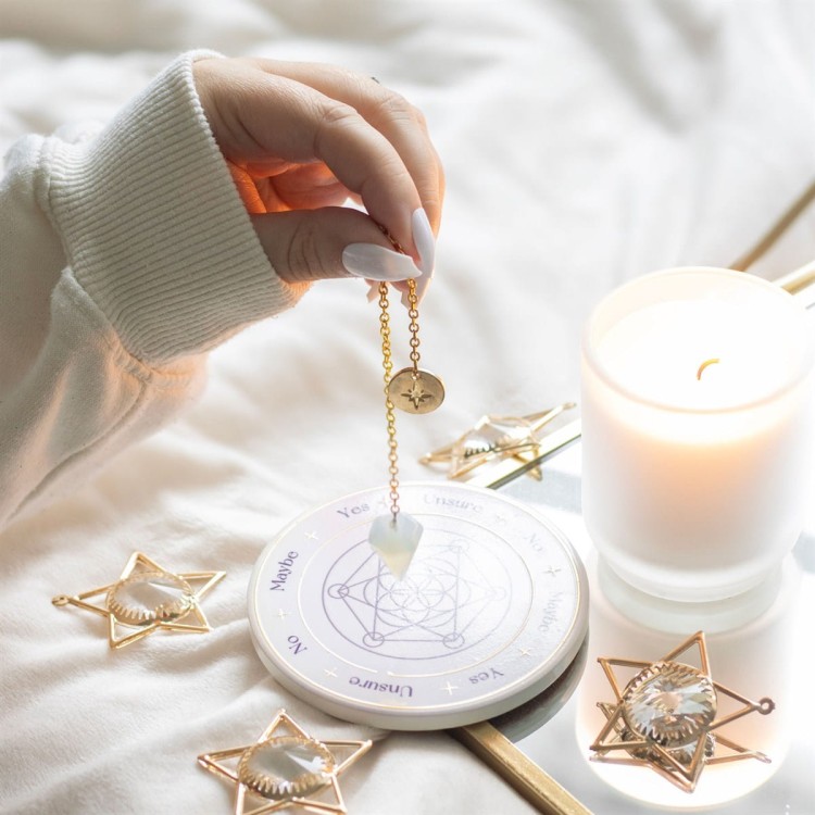 Osoba używająca wahadełka z opalitu nad tablicą do dywinacji przy świecy