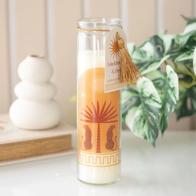 Świeca Sandalwood &amp; Oud w dekoracyjnej tubie ustawiona na stoliku obok roślin.